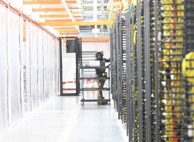 Trabajador de TI inspecciona servidores en una gran granja de servidores con acentos e iluminación brillante